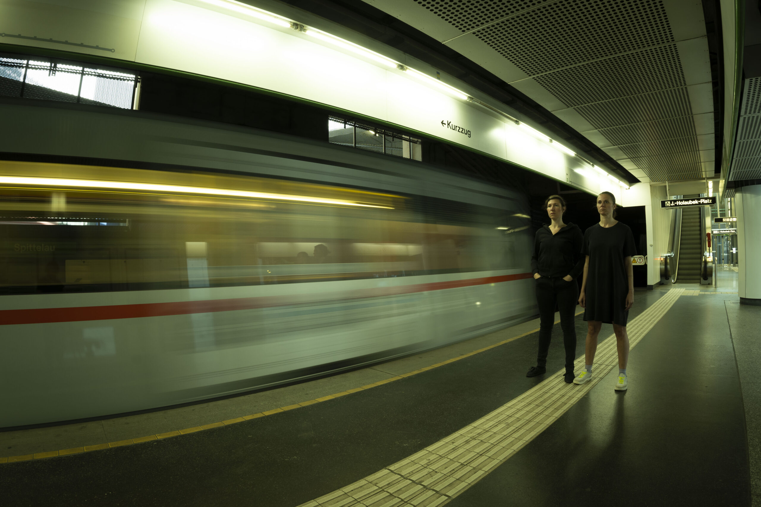 A train driving through a subway station. two persons standing on the quai and looking at the camera.